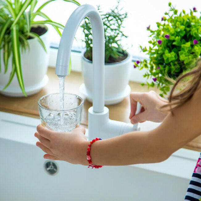 Children picks up a glass of water from the tap. Selective focus. Kid.